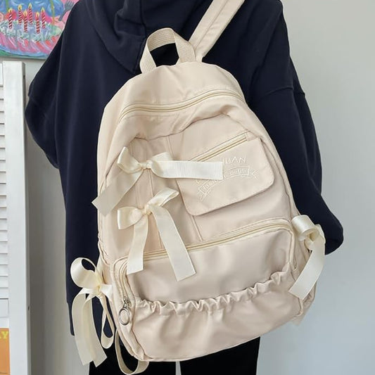 Beige backpack with ribbons held by a person against a neutral background