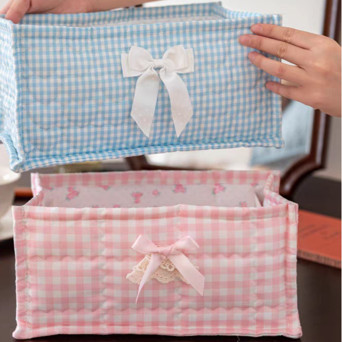Two fabric storage boxes with checkered patterns and ribbons, held open by a hand.